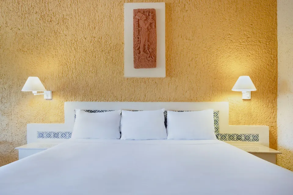 Close-up of a king bed with textured wall and bedside lamps in a room at Iberostar Waves Tucán