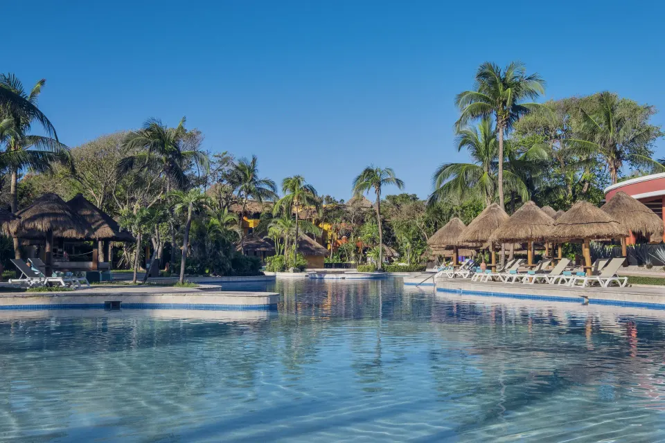 Resort pool lined with palapas, palm trees, and lounge chairs at Iberostar Waves Tucán