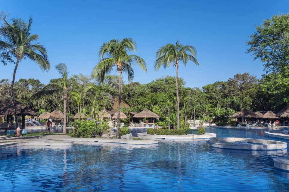 Blue resort pool with tall palms and palapas on the far side at Iberostar Waves Tucán