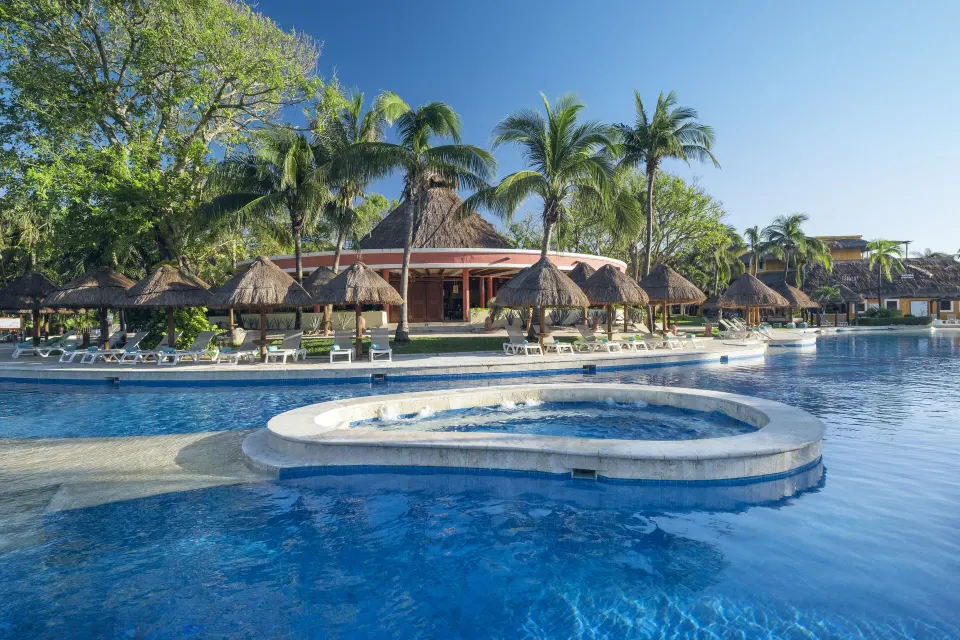 Curved pool edge and raised circular splash area with palapas in background at Iberostar Waves Tucán