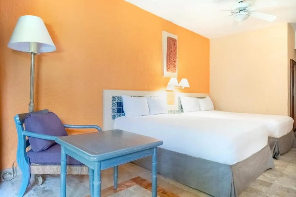 Corner of a guest room showing two beds, a blue chair, table and floor lamp at Iberostar Waves Tucán