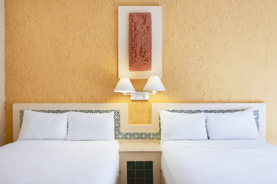 Two double beds framed by textured wall art and bedside lamp at Iberostar Waves Tucán