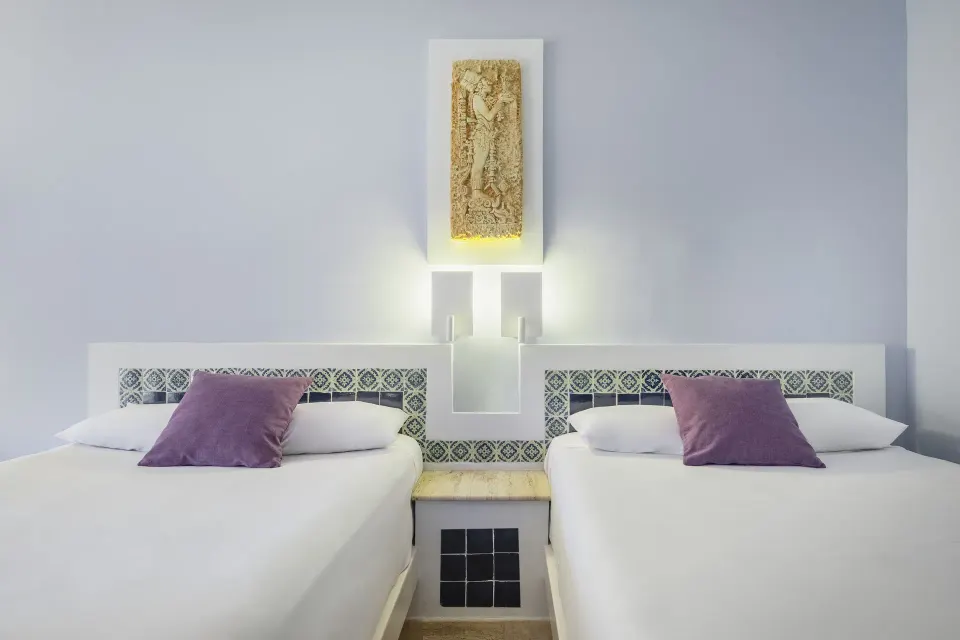 Head-on view of two twin beds with patterned headboard and purple accent cushions at Iberostar Waves Tucán