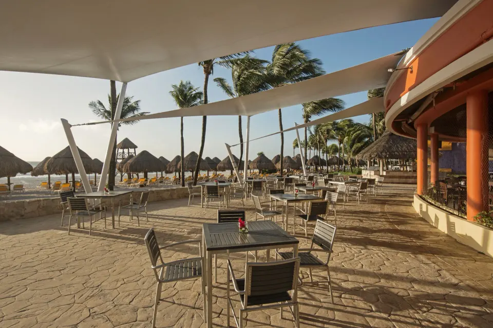 Outdoor beachfront dining terrace with tables and palapas at Iberostar Waves Tucán