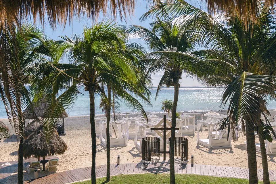 Oceanfront Junior Suite at Iberostar Waves Tucán showing palm trees, beach cabanas and the sparkling sea.