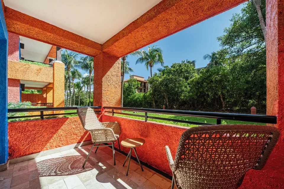 Balcony with two wicker chairs and table at Iberostar Waves Tucán, looking toward garden