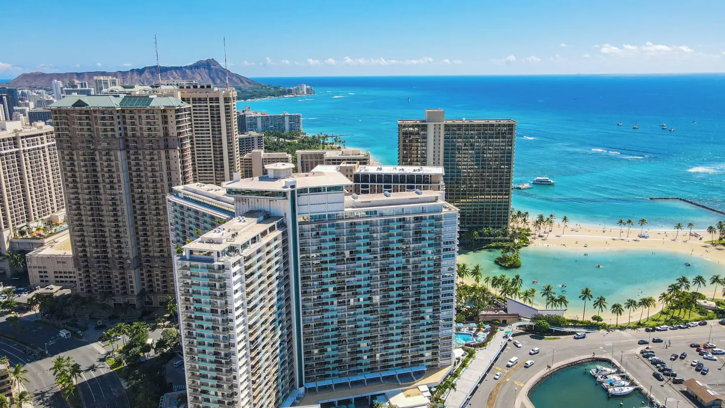 Aerial view of Ilikai Hotel beside Waikiki beach, lagoon, marina, and blue ocean.