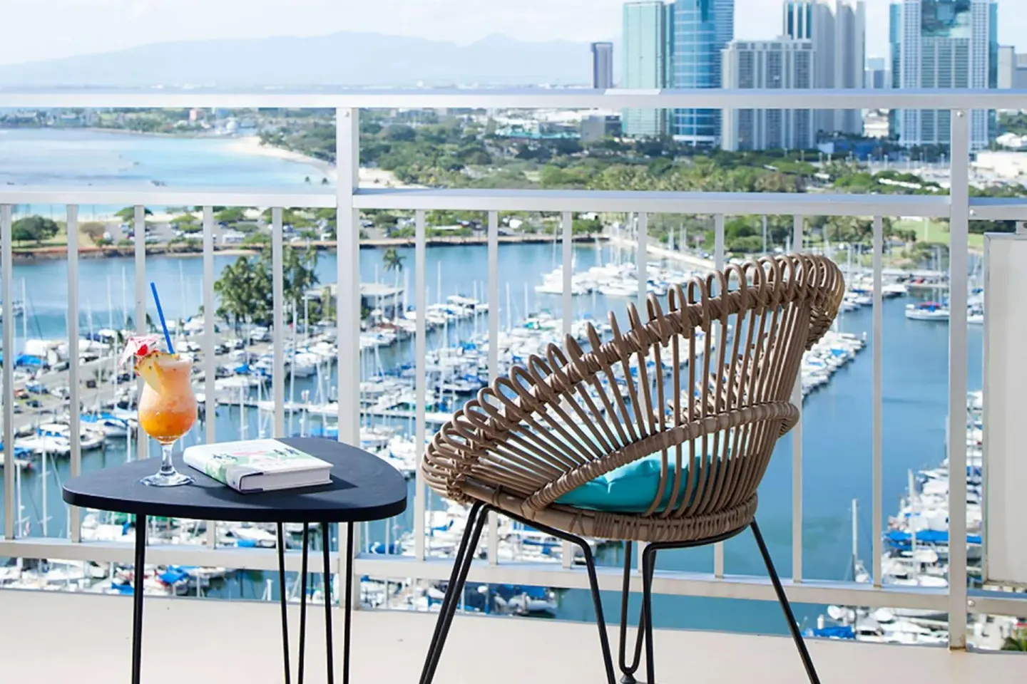 Balcony at Ilikai Hotel with a chair, table, drink, and marina and city views.