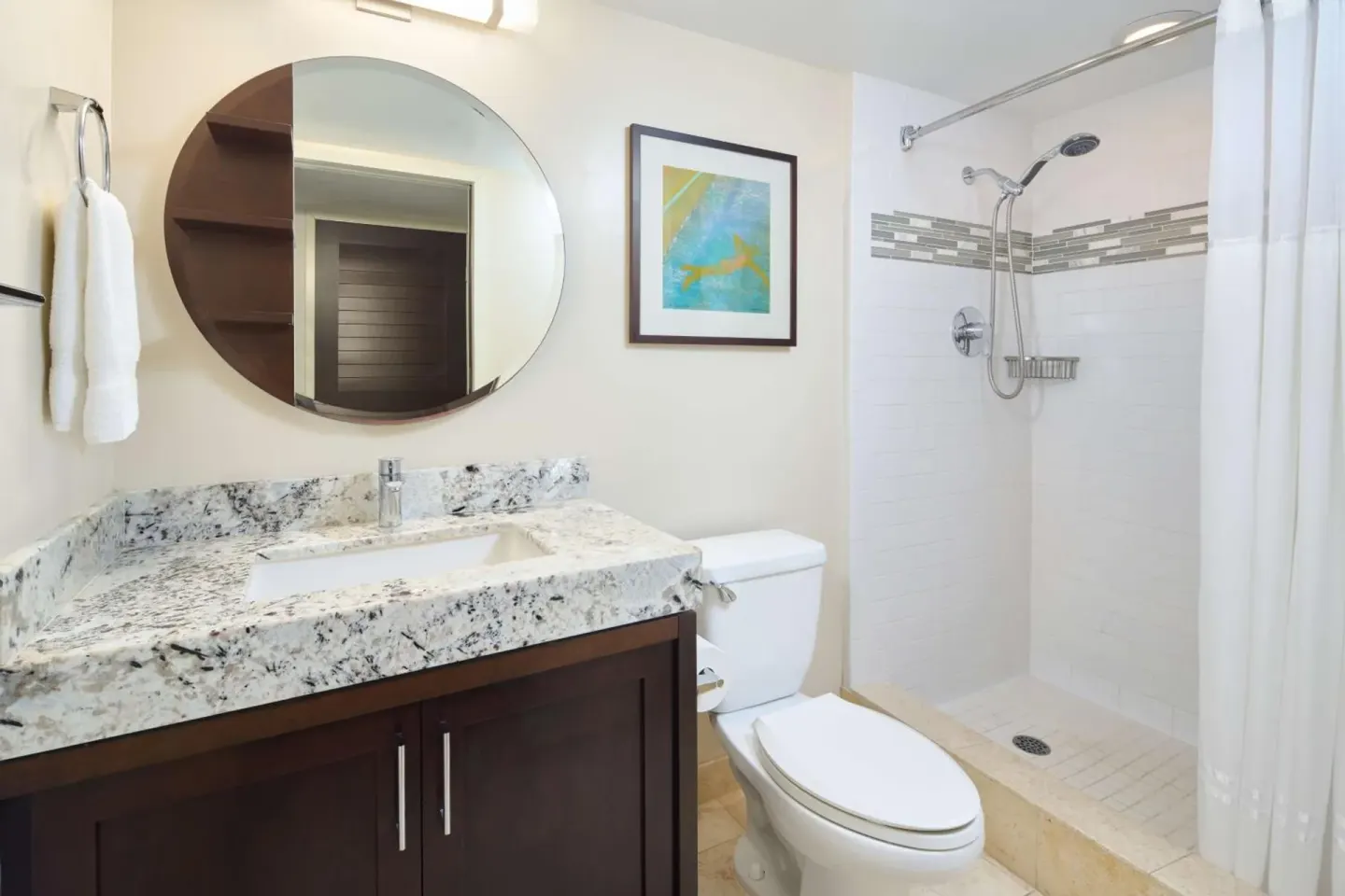 Bathroom with round mirror, granite vanity, toilet, and shower at Ilikai Hotel.