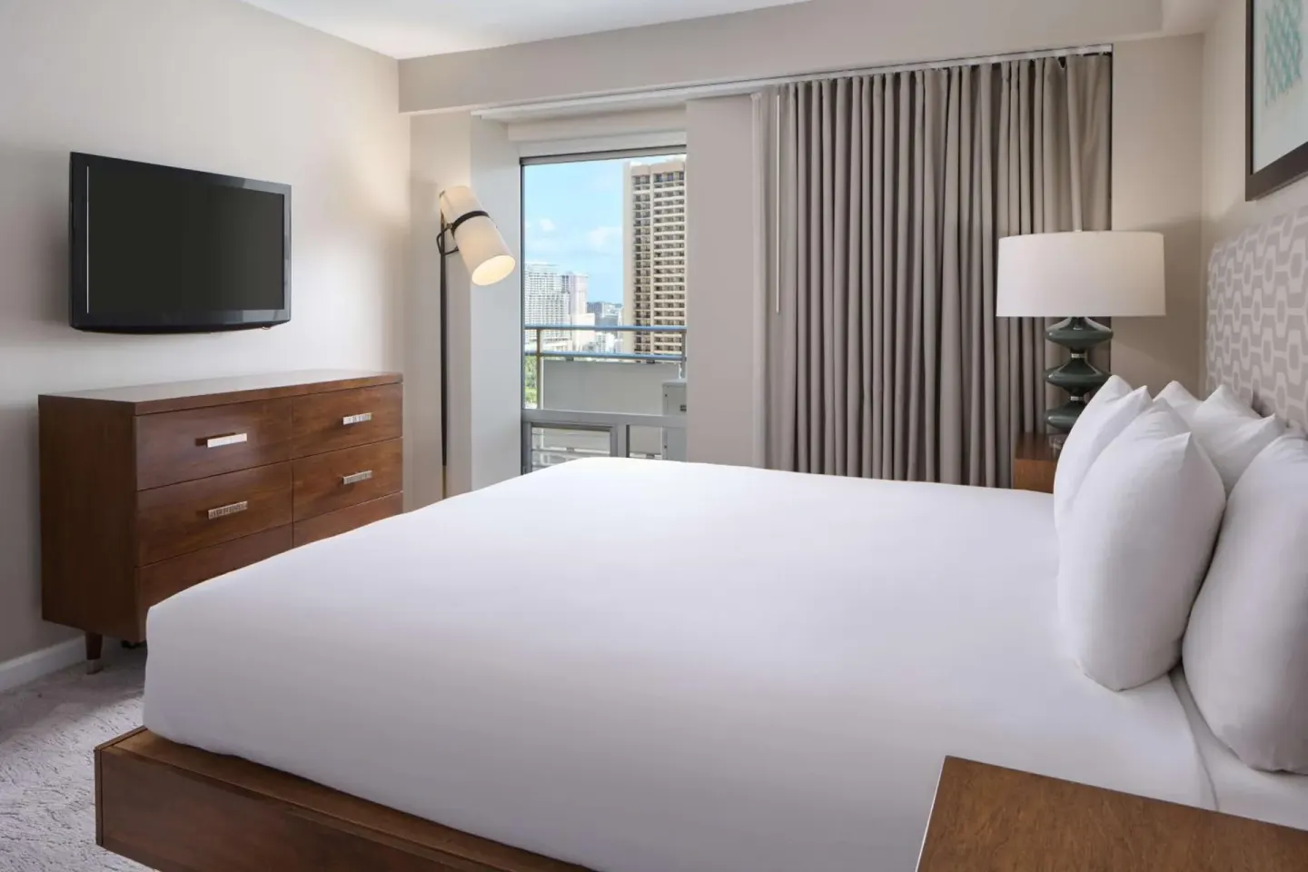 King bed guest room with wall TV, dresser and balcony doorway at Ilikai Hotel.