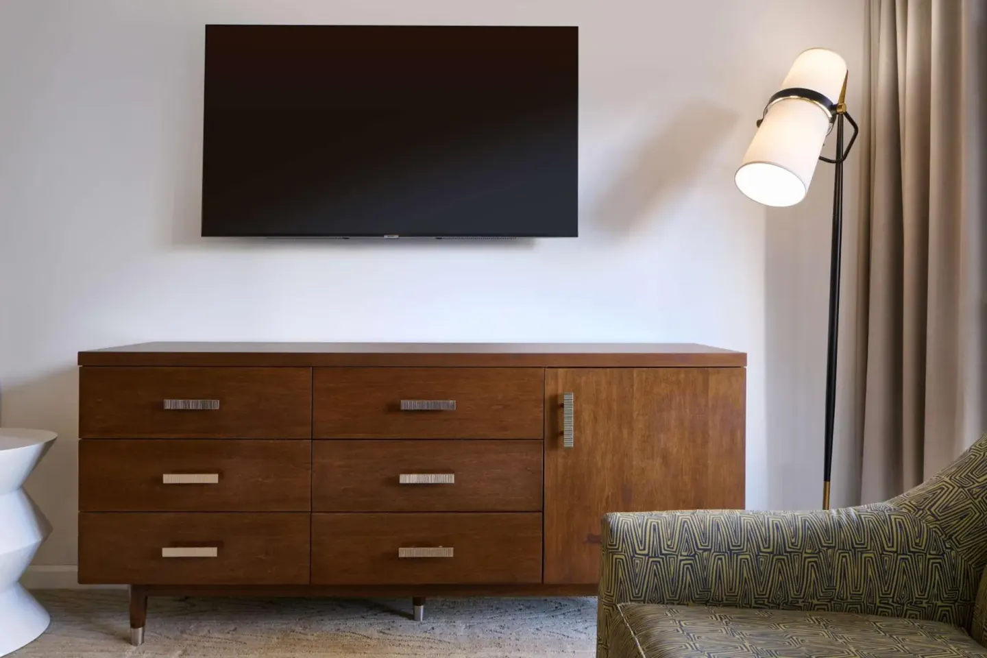 Guest room dresser area at Ilikai Hotel with wall-mounted TV, floor lamp, and patterned chair.
