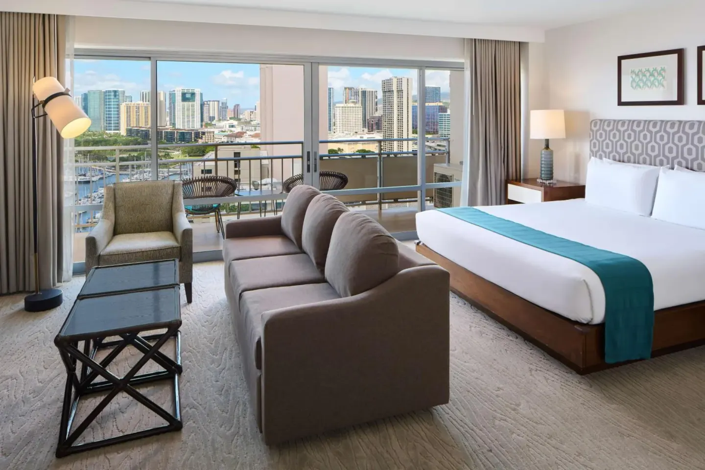 Guest room with king bed, sofa, armchair, and balcony marina view at Ilikai Hotel.