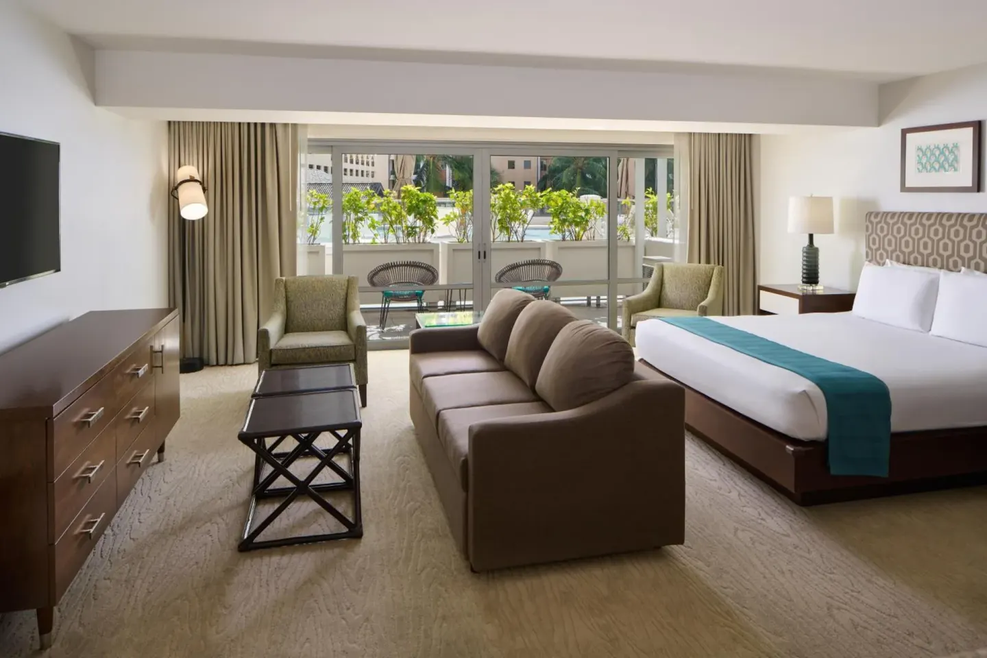 Guest room with king bed, sofa, TV, and terrace seating at Ilikai Hotel.