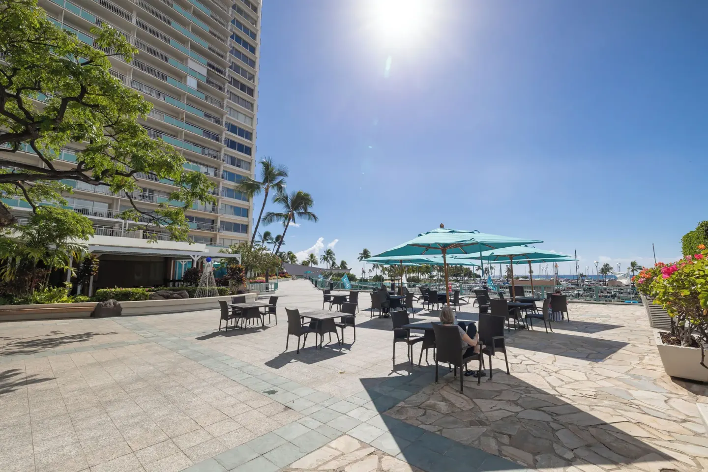 Outdoor patio with café tables, teal umbrellas, and marina views at Ilikai Hotel.
