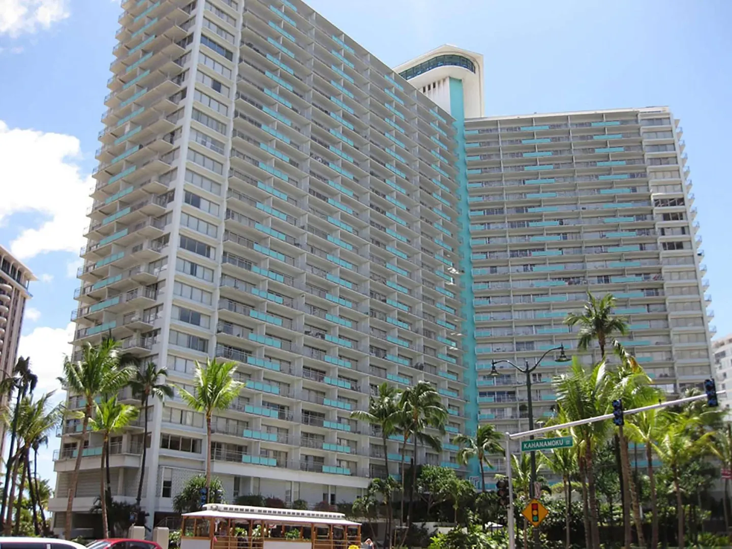 Street-level view of the Ilikai Hotel tower with balconies, palm trees, and a trolley.