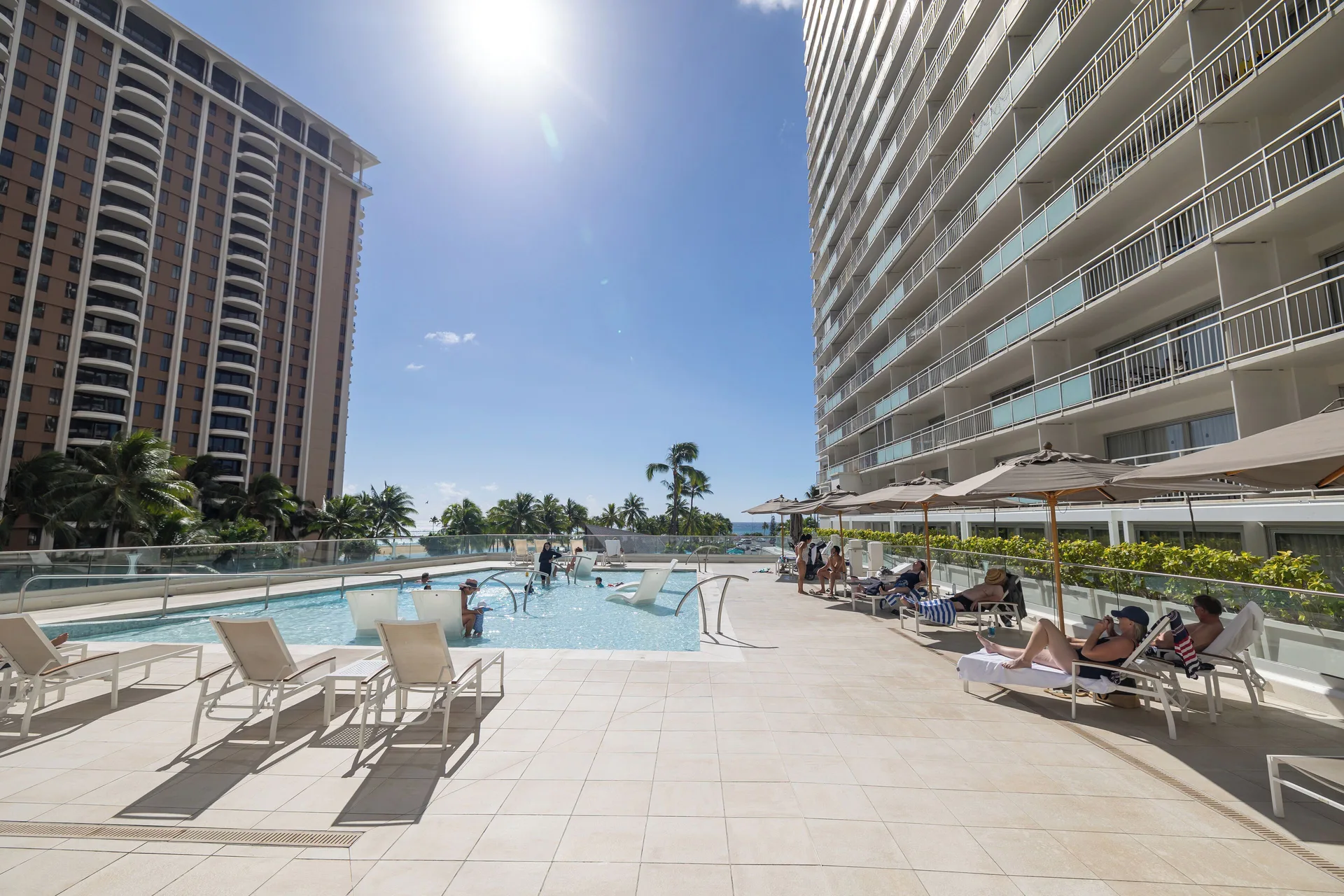 Sunny pool deck with lounge chairs beside the Ilikai Hotel tower.
