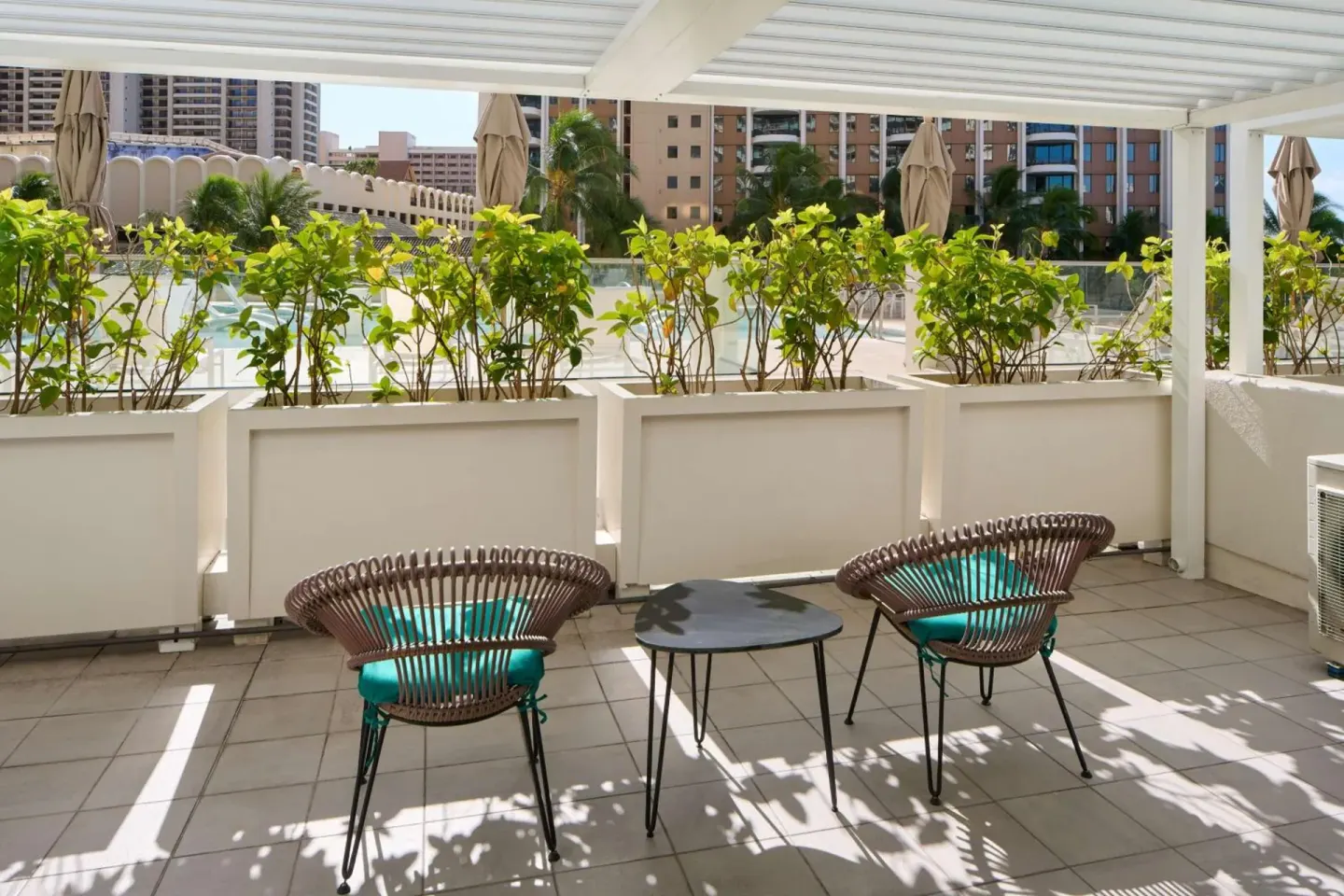 Terrace seating at Ilikai Hotel with two woven chairs, a small table, planters, and shade.