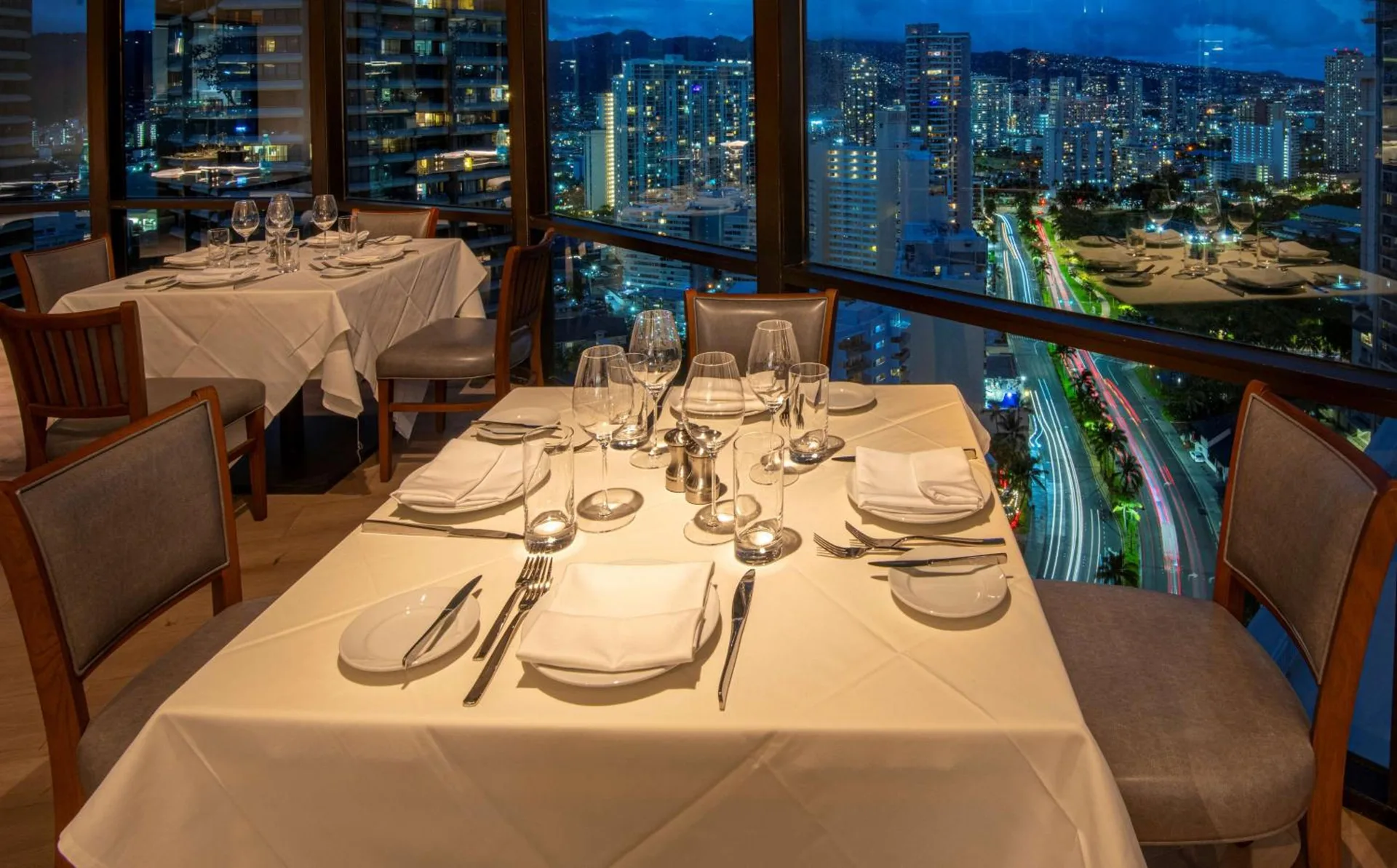 Window-side restaurant tables with nighttime city views at Ilikai Hotel.