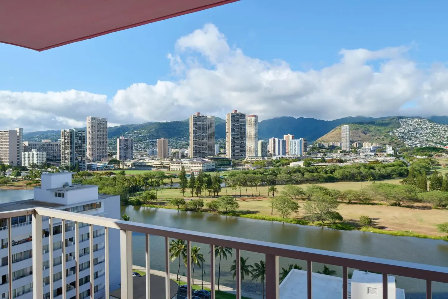 Balcony view from Ilima Hotel toward a canal, city skyline, and green mountains.