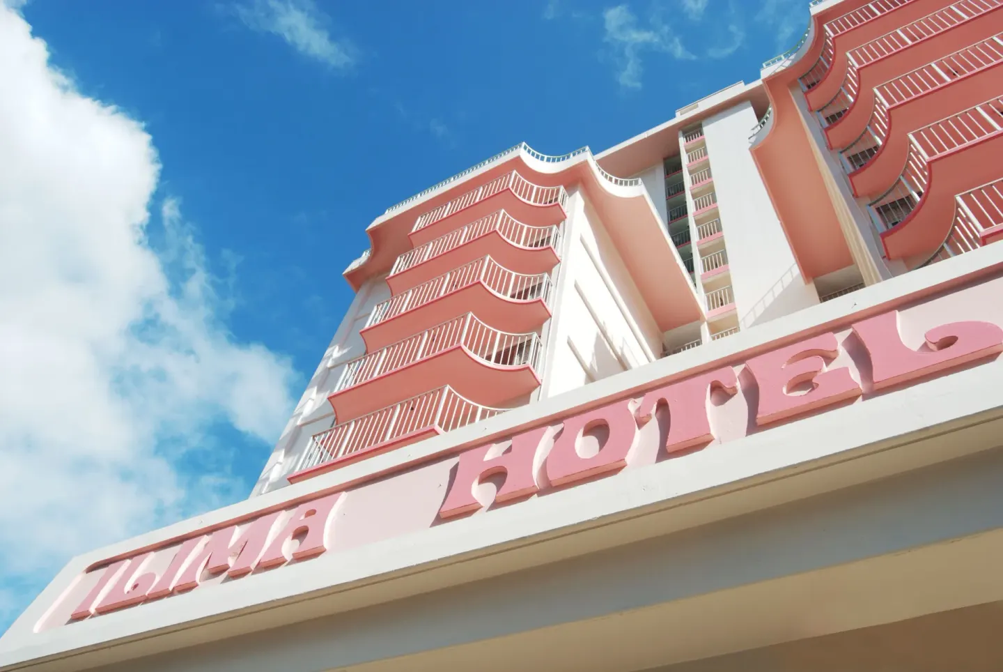 Low-angle view of the pink-and-white exterior and sign at Ilima Hotel.
