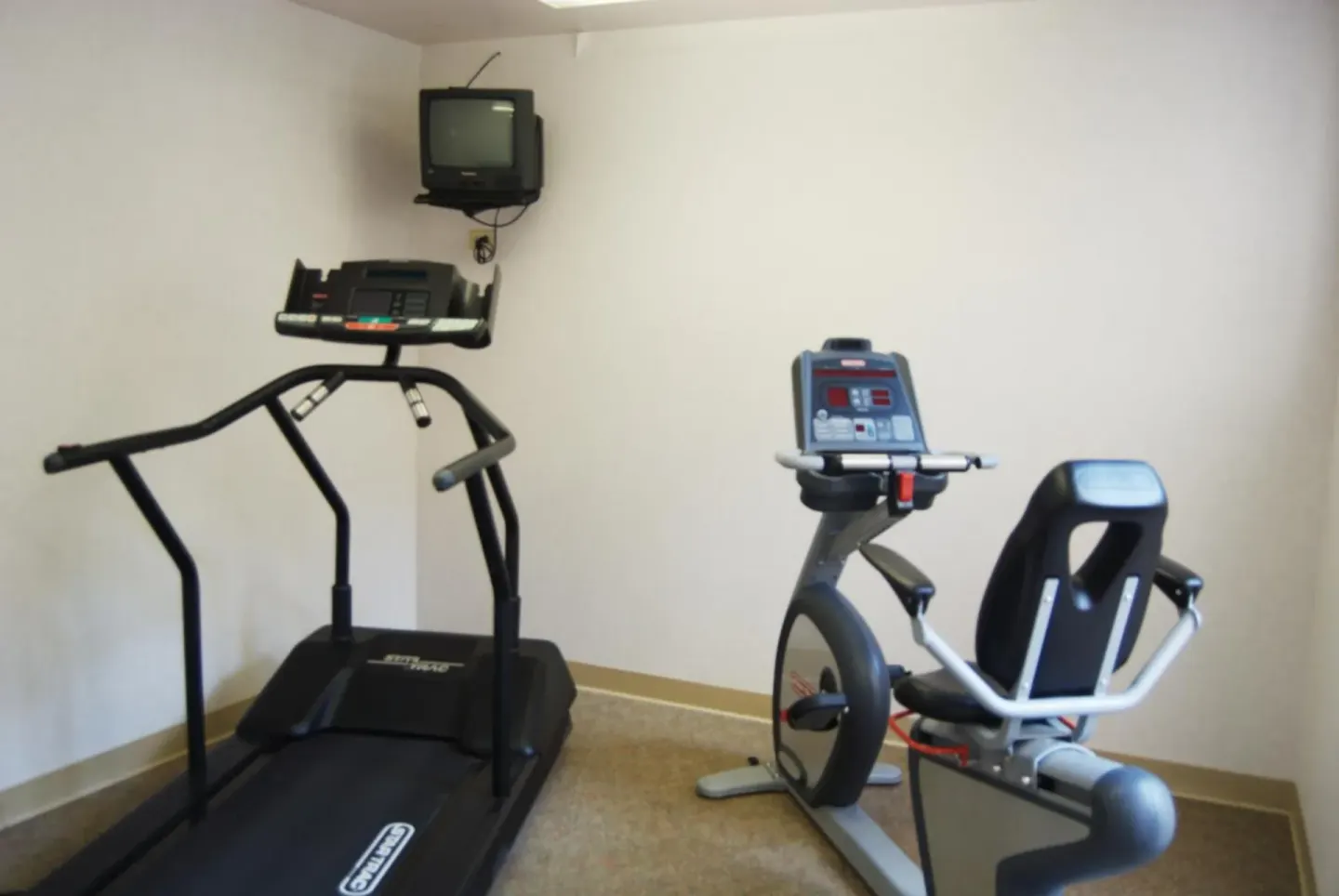 Small fitness room with treadmill, exercise bike, and wall-mounted TV at Ilima Hotel.