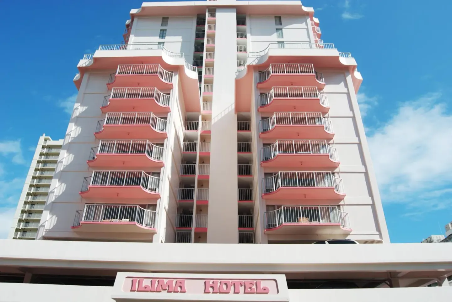 Front exterior of Ilima Hotel with pink balconies and hotel sign.