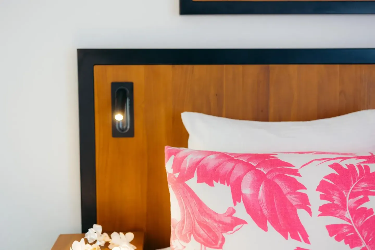 Close-up of a bed pillow and wooden headboard with reading light at Ilima Hotel.
