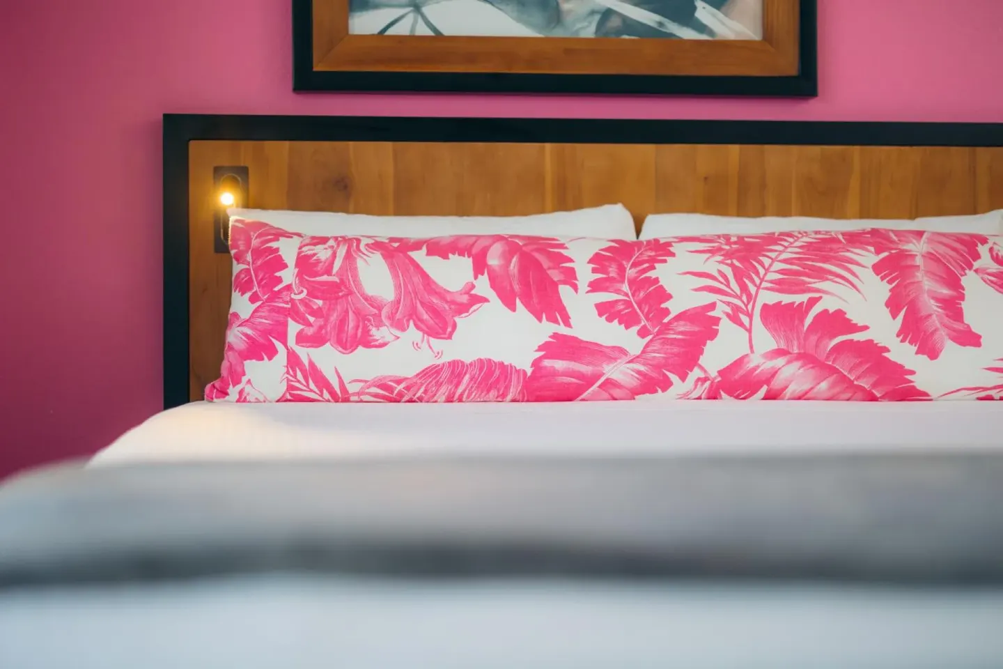 Bed with pink tropical pillows and a wood headboard in a guest room at Ilima Hotel.