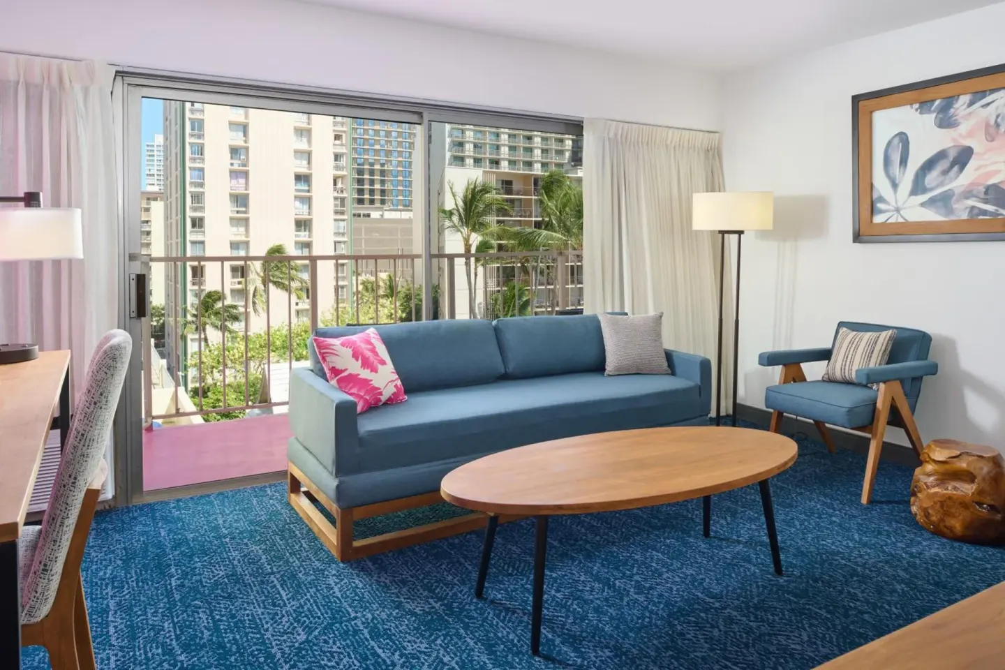 Guest room sitting area at Ilima Hotel with blue sofa, chair, table, and balcony doors.