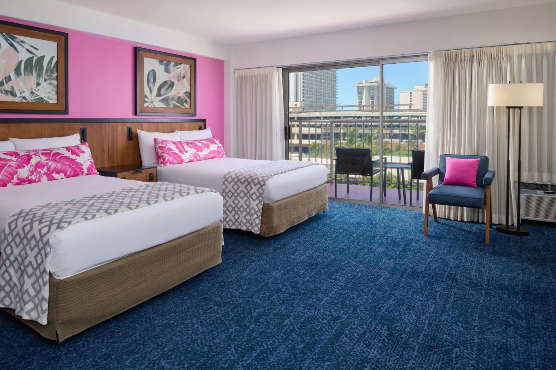 Two beds and balcony seating in a bright guest room at Ilima Hotel.