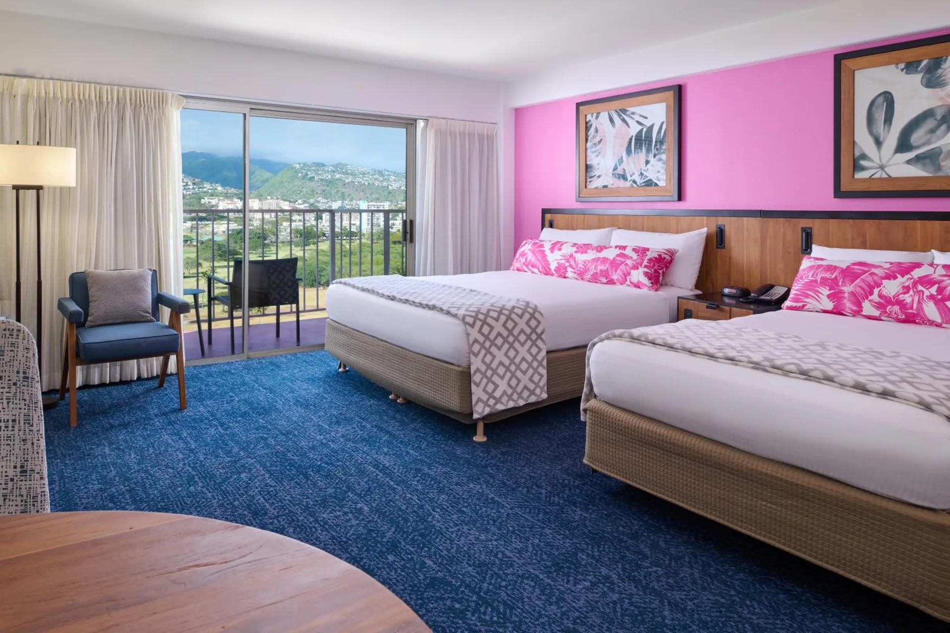 Two beds, blue carpet, and a balcony with mountain views in a guest room at Ilima Hotel.