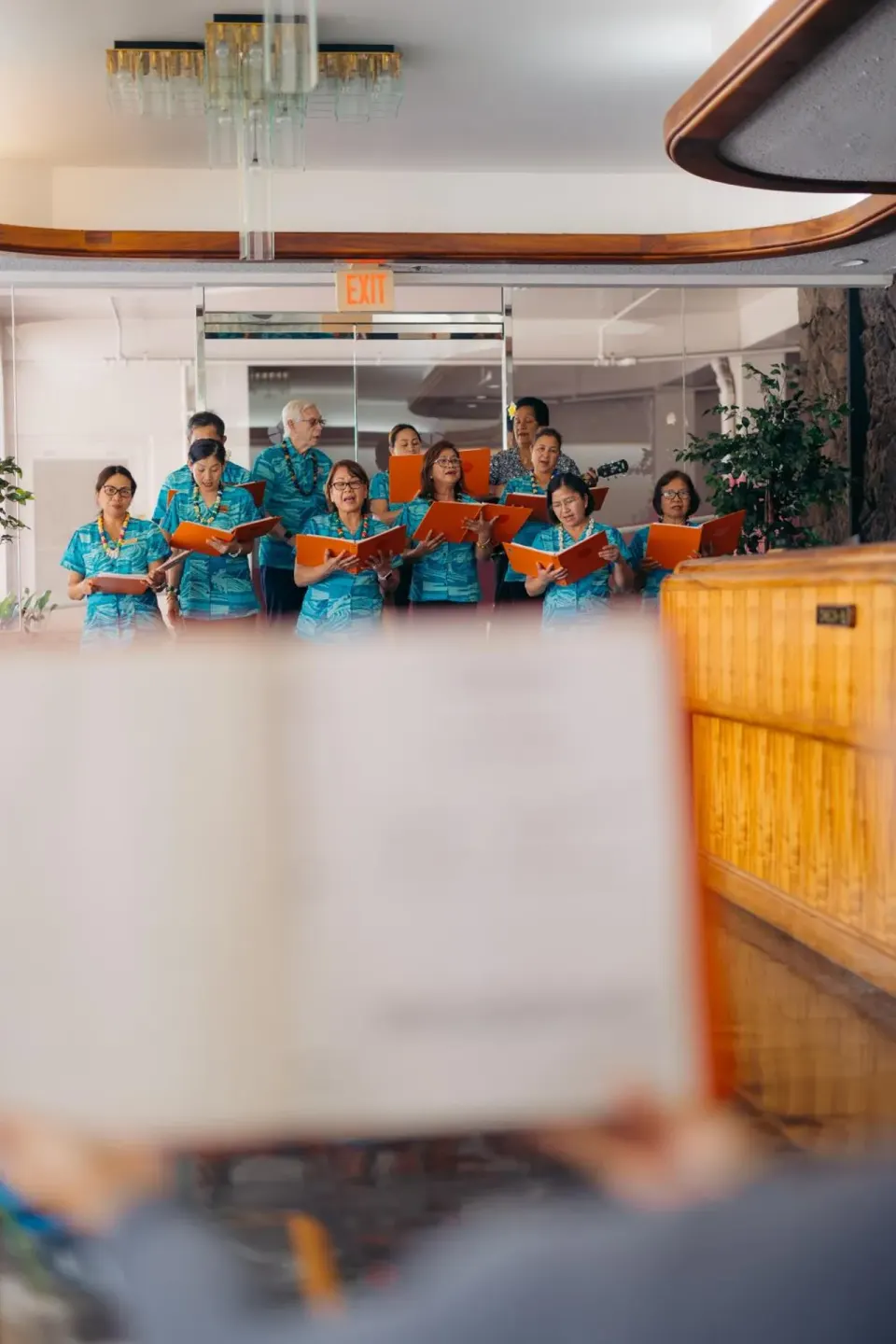 Choir members sing with orange folders in the lobby at Ilima Hotel.