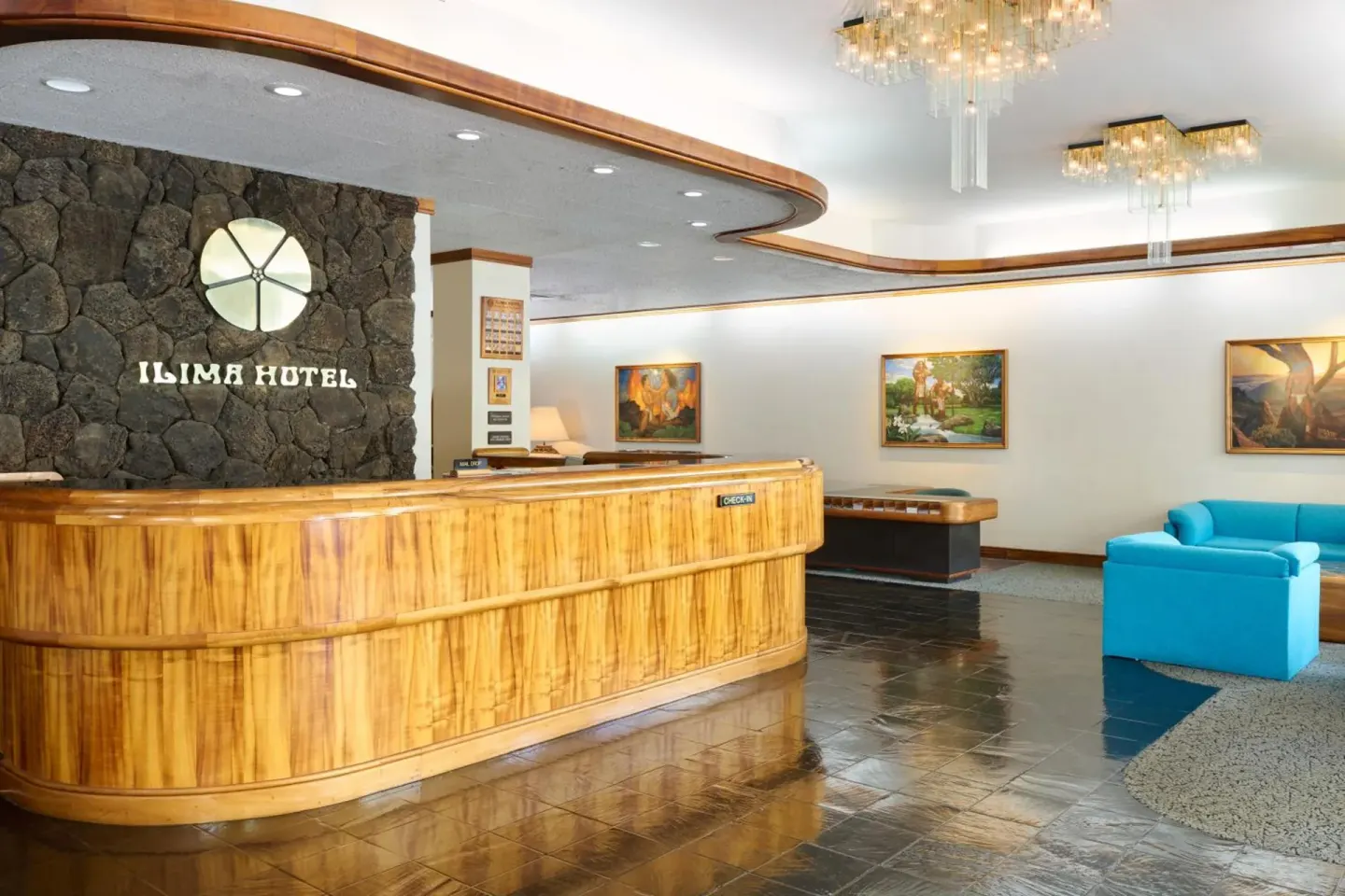 Lobby front desk at Ilima Hotel with wood counter, stone wall, and blue seating.