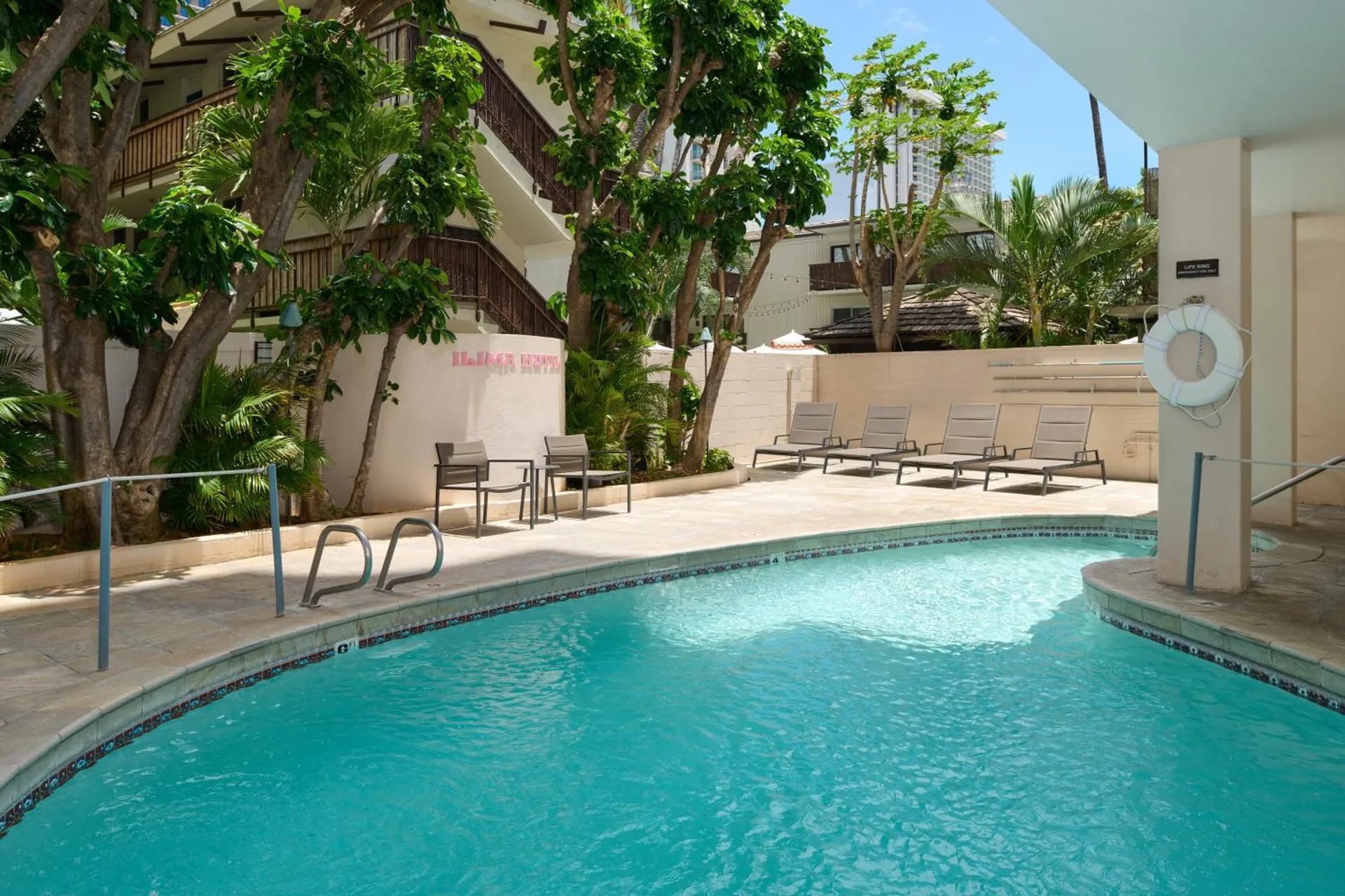 Outdoor swimming pool with lounge chairs and tropical trees at Ilima Hotel.