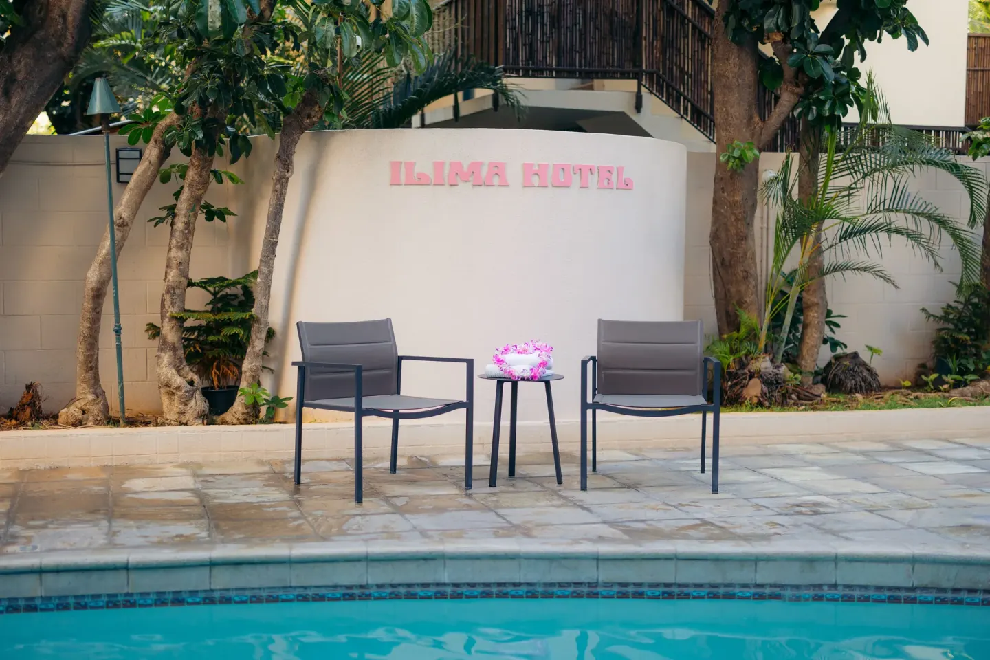 Poolside chairs and table in front of the Ilima Hotel sign.