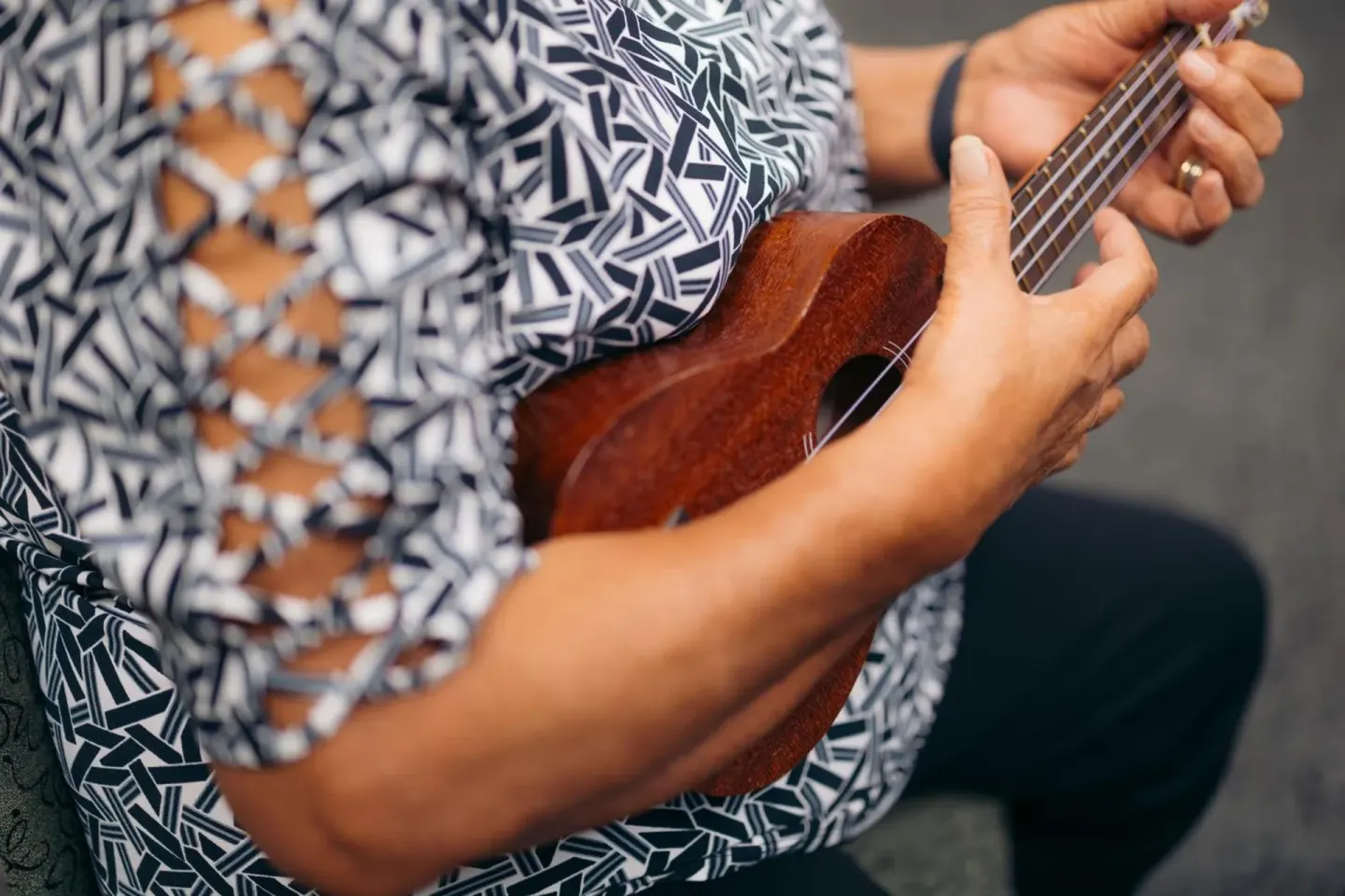 Close-up of hands playing a wooden ukulele at Ilima Hotel.