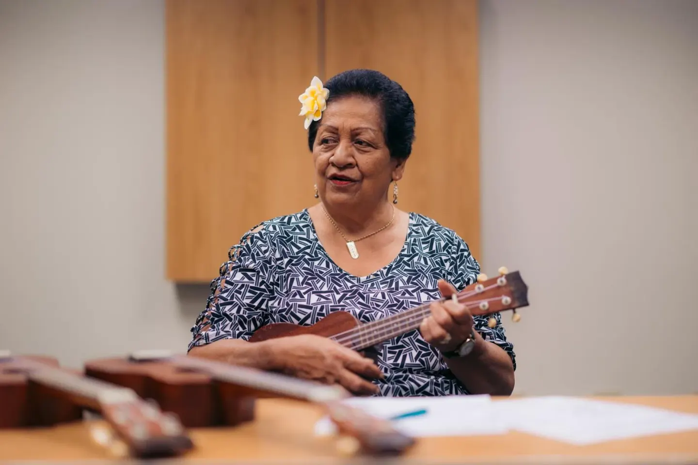 Ukulele player with a flower in her hair seated indoors at Ilima Hotel.