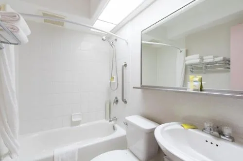 Deluxe Studio bath area with white tub, shower wand, and vanity at Ilima Hotel.