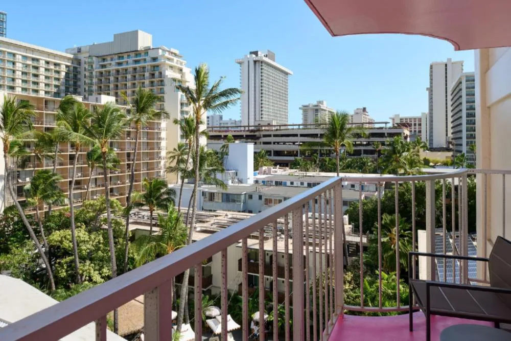 Balcony view with railing, chair, palm trees, and city buildings at Ilima Hotel.