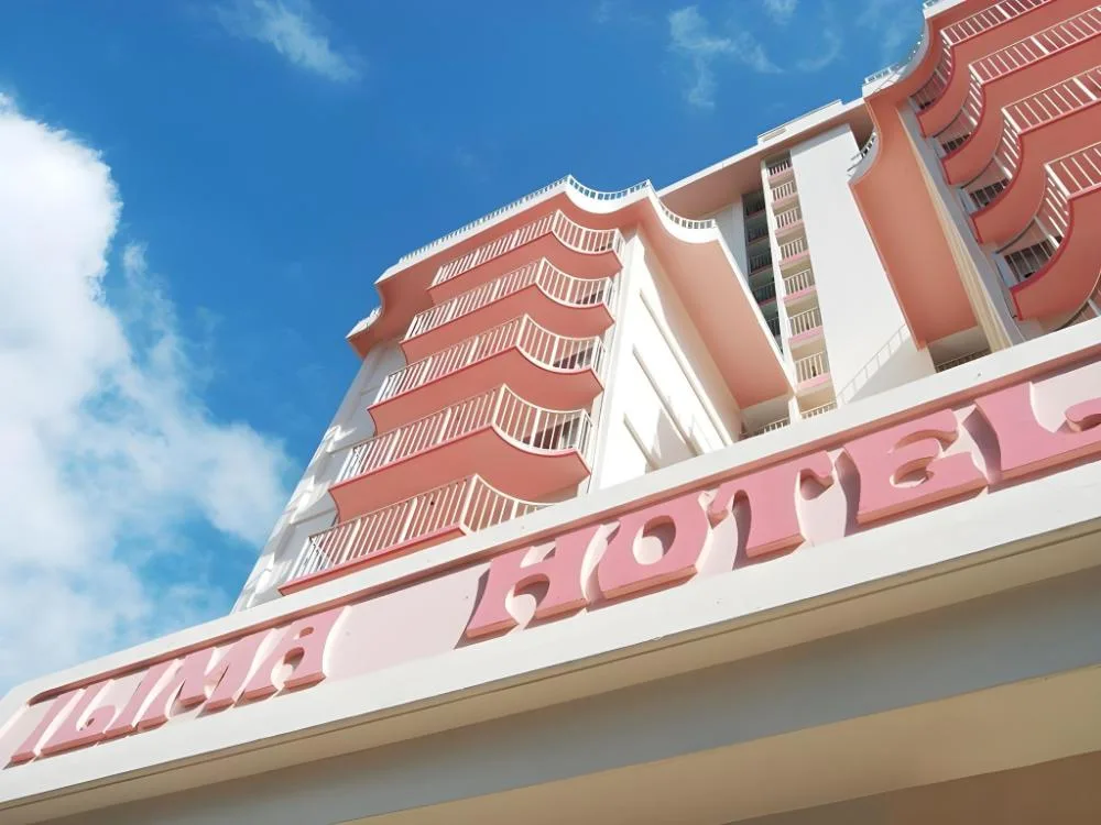 Low-angle view of the pink exterior balconies and Ilima Hotel sign against a blue sky.