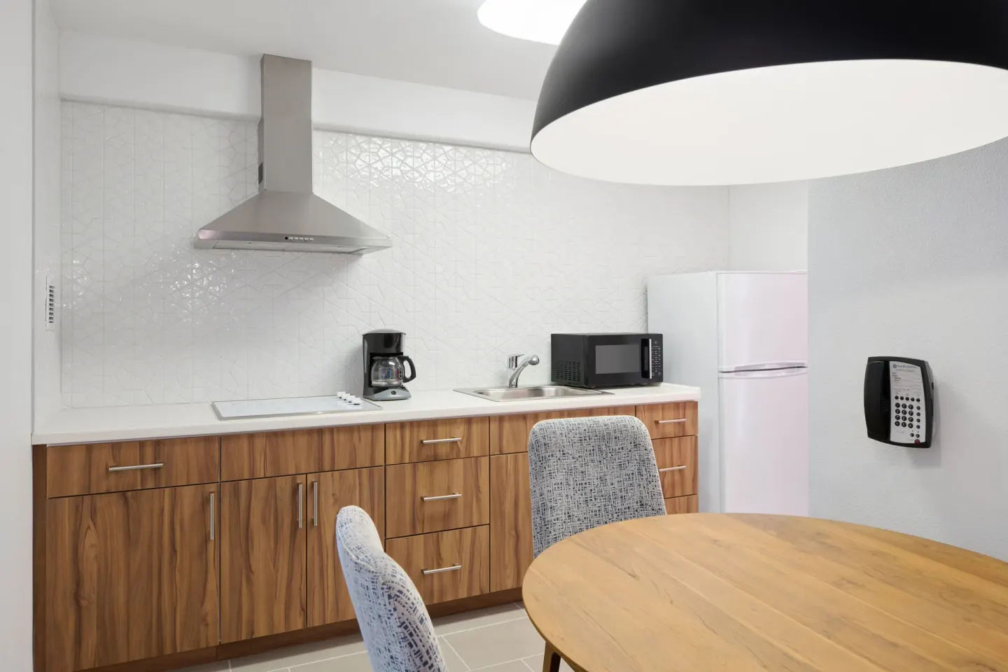Suite kitchen with wood cabinets, refrigerator, microwave, sink, and dining table at Ilima Hotel.