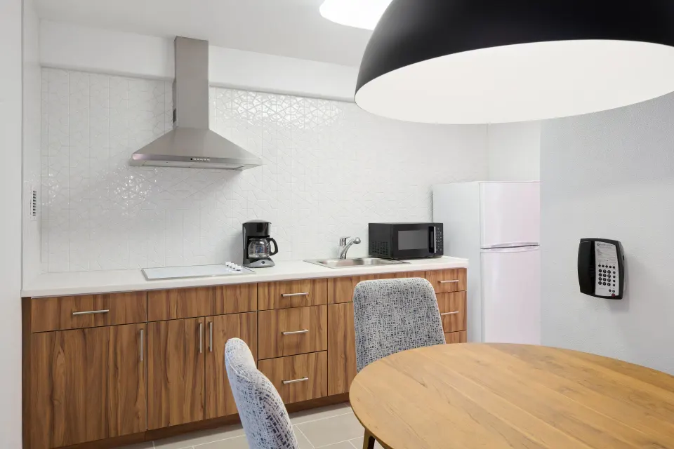Suite kitchen with wood cabinets, refrigerator, microwave, sink, and dining table at Ilima Hotel.