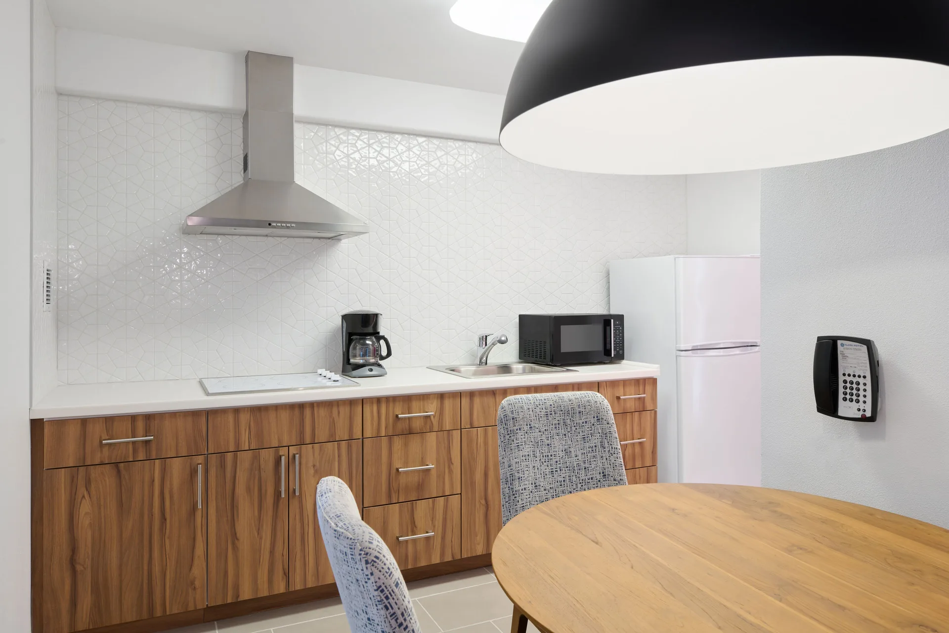 Suite kitchen with wood cabinets, refrigerator, microwave, sink, and dining table at Ilima Hotel.