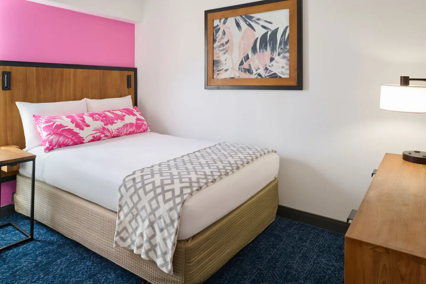 Bedroom with a single bed, pink accent wall, framed art, and dresser in a suite at Ilima Hotel.