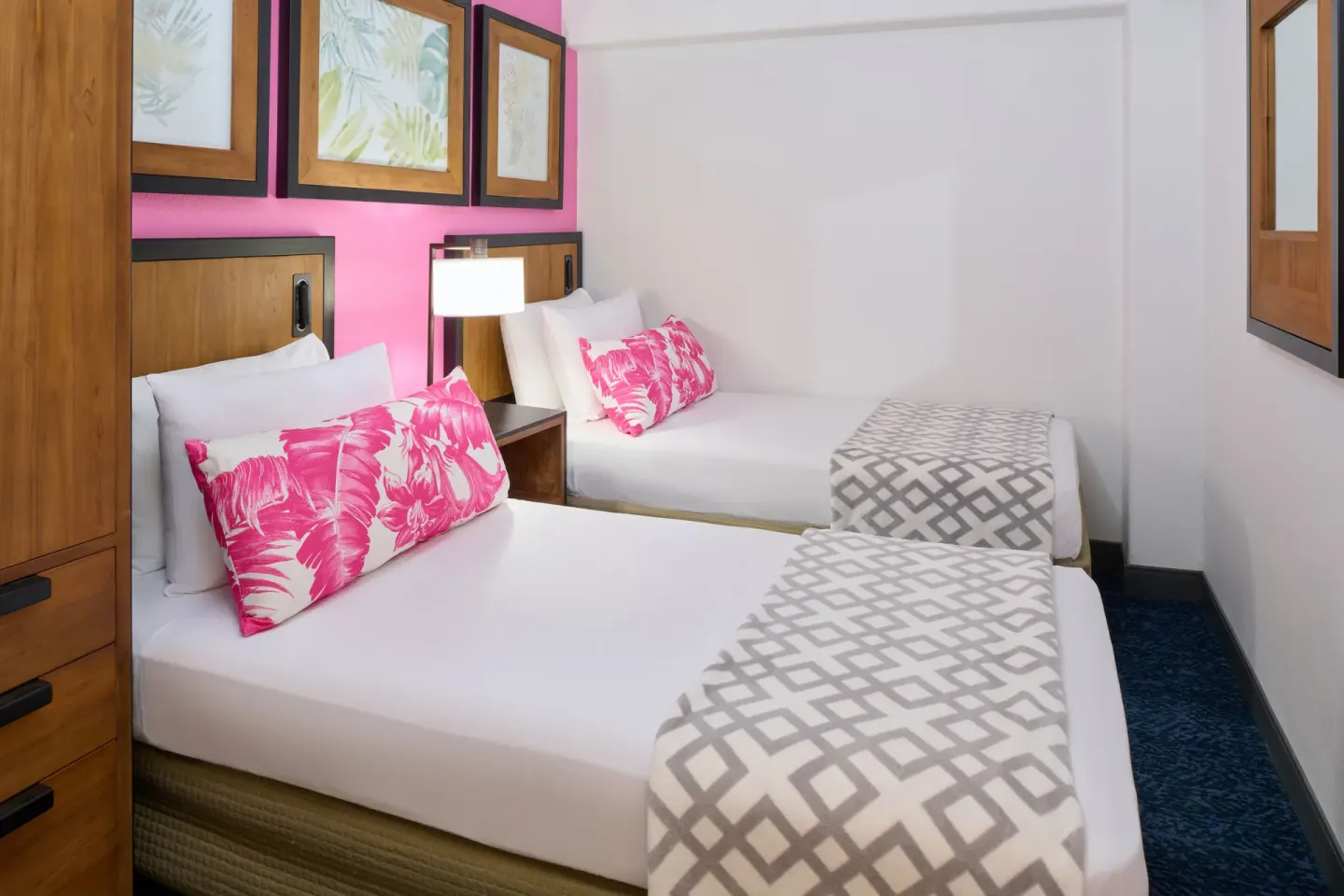 Suite bedroom with two beds, pink pillows, wall art, and a mirror at Ilima Hotel.