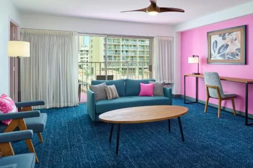 Two Bedroom Suite seating area with sofa, desk, and pink wall at Ilima Hotel.