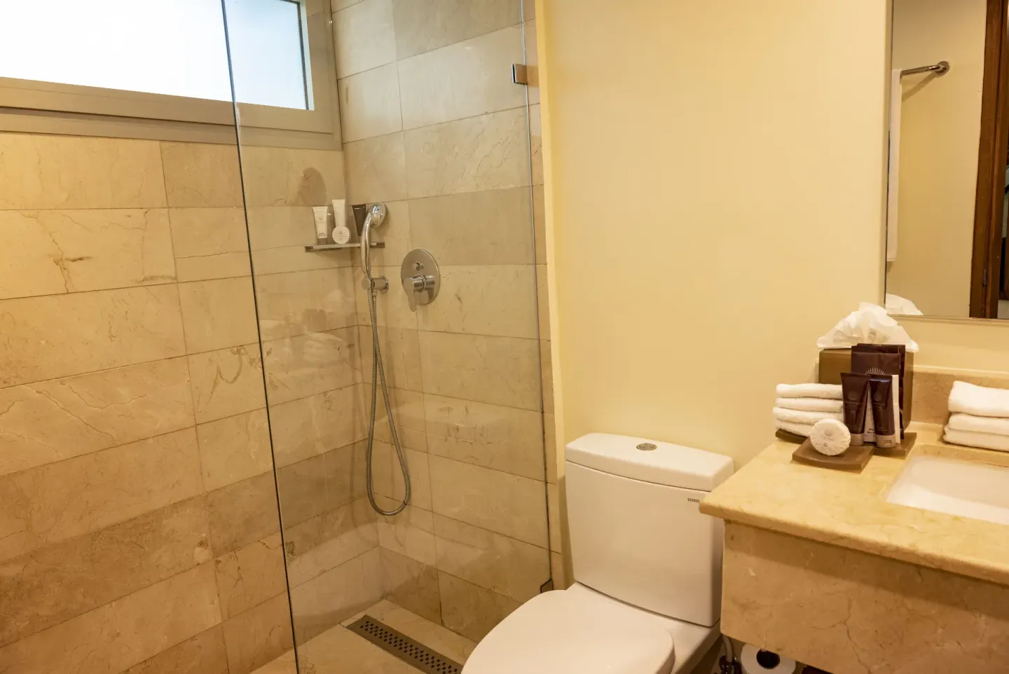 Bathroom with glass shower, toilet, vanity, towels, and amenities at Impressive Premium Punta Cana.