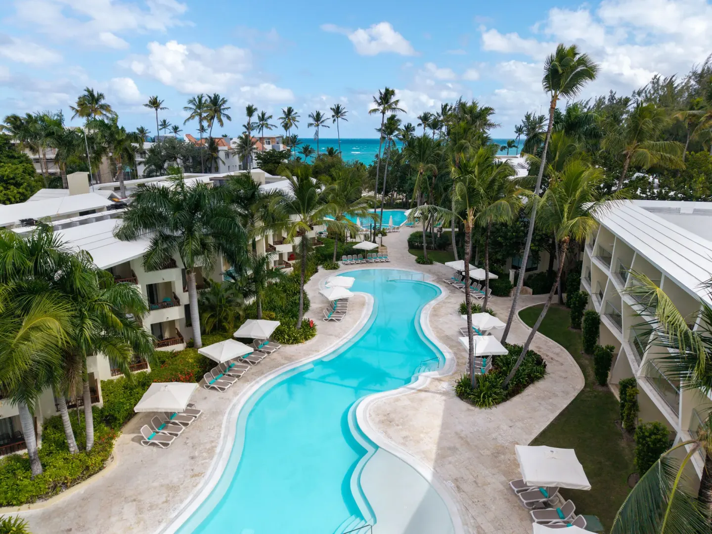 Long winding pool between resort buildings and palms at Impressive Premium Punta Cana.