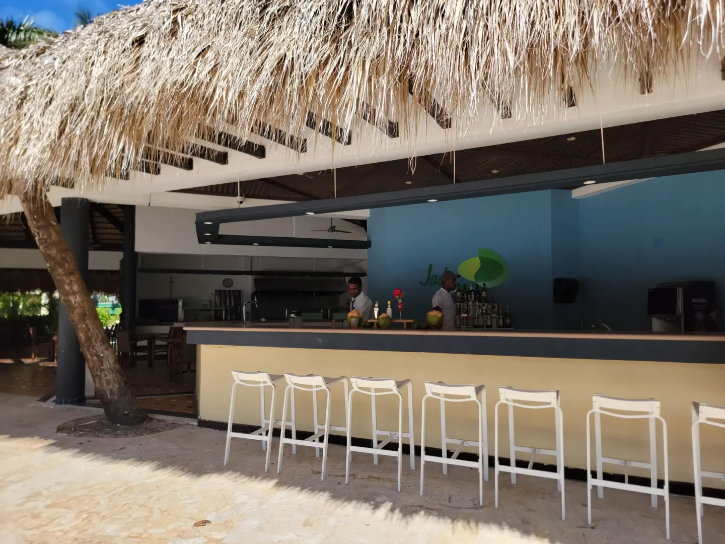 Open-air resort bar with white stools beneath a thatched roof at Impressive Premium Punta Cana.