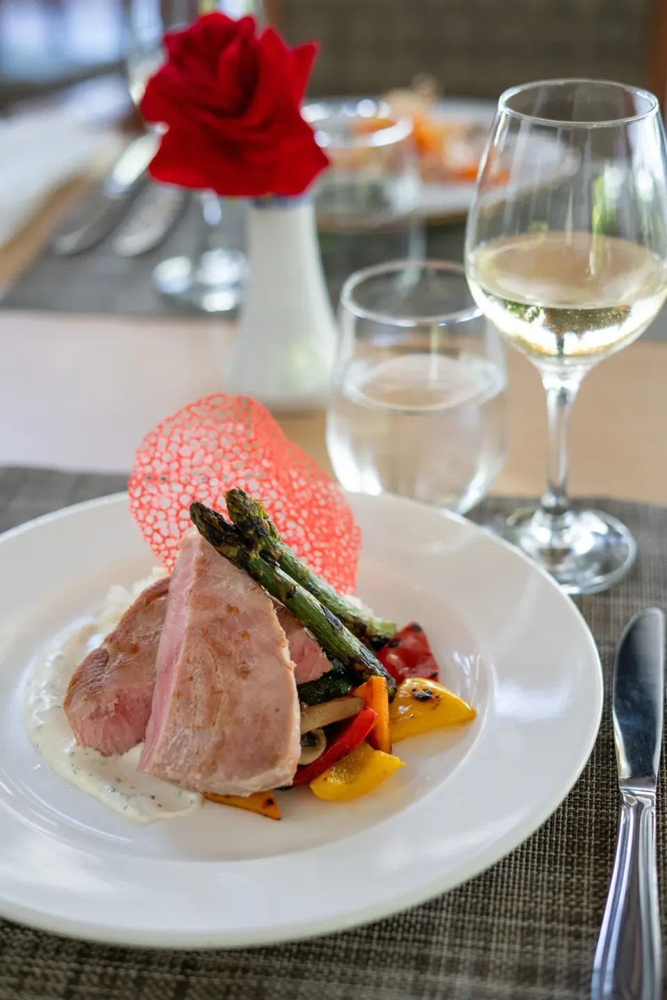 Plated entrée with wine, water, and a red rose at Impressive Premium Punta Cana.